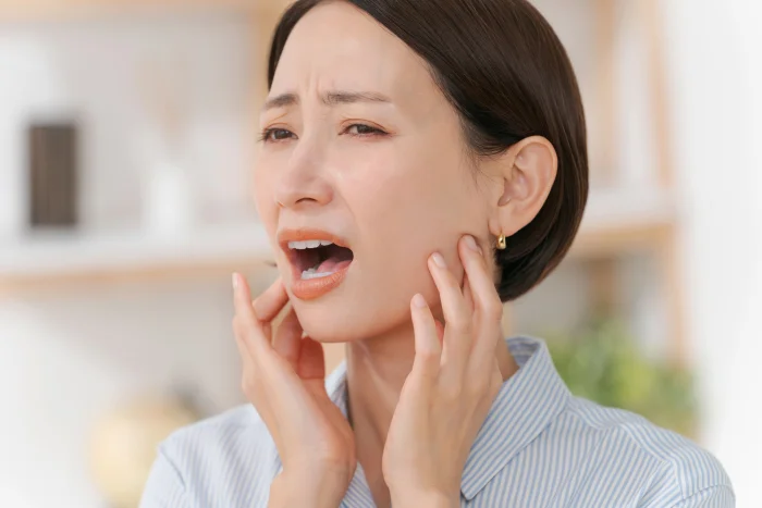口が開けにくく顎を押さえる女性